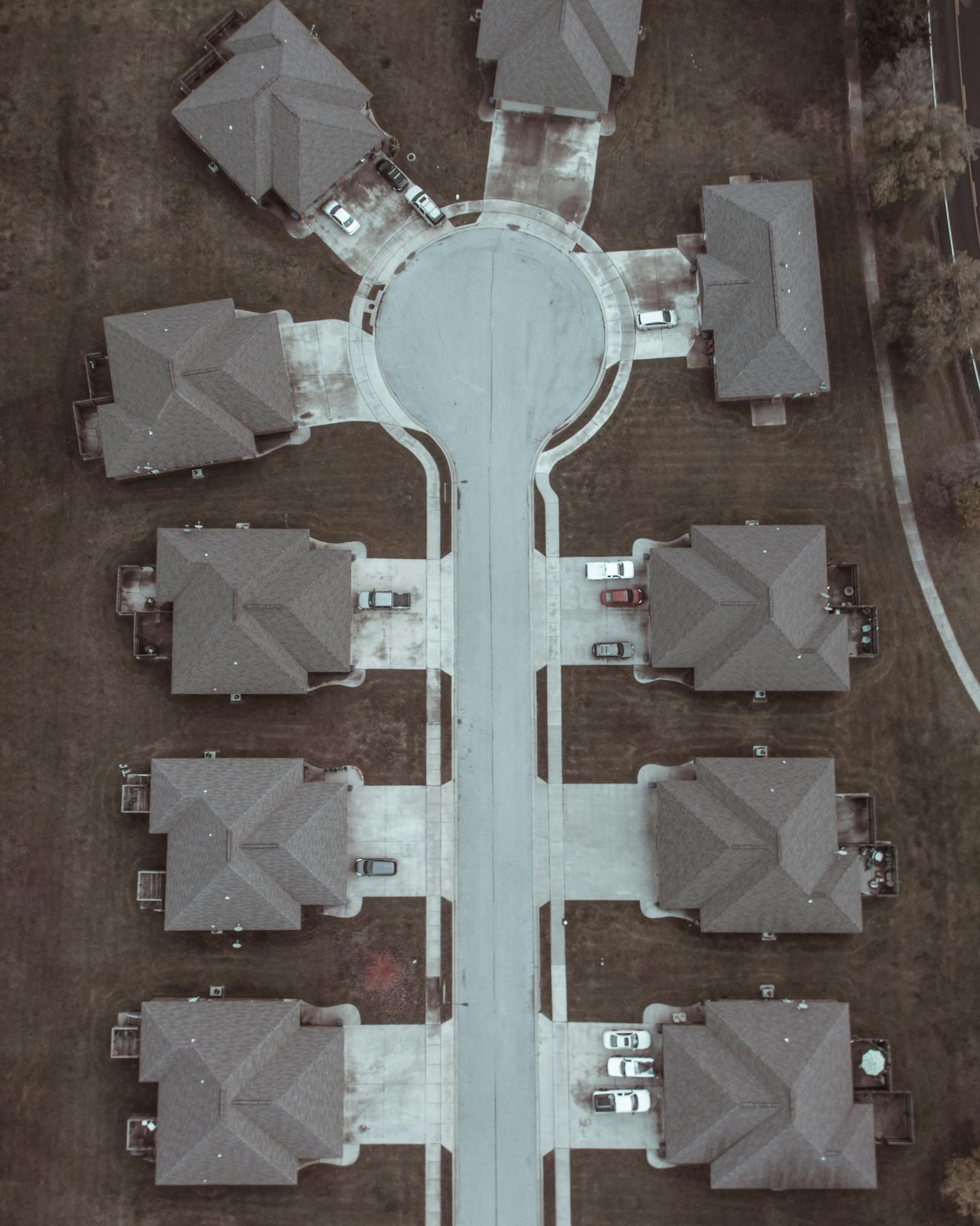 Aerial shot of a suburban cul-de-sac with identical houses and parked cars.